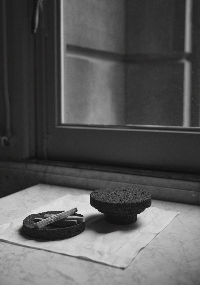 Elevated Sculptural Tray: Handcrafted lava stone tray with a shallow bowl holding slender wooden sticks, set on an inverted stone pedestal.