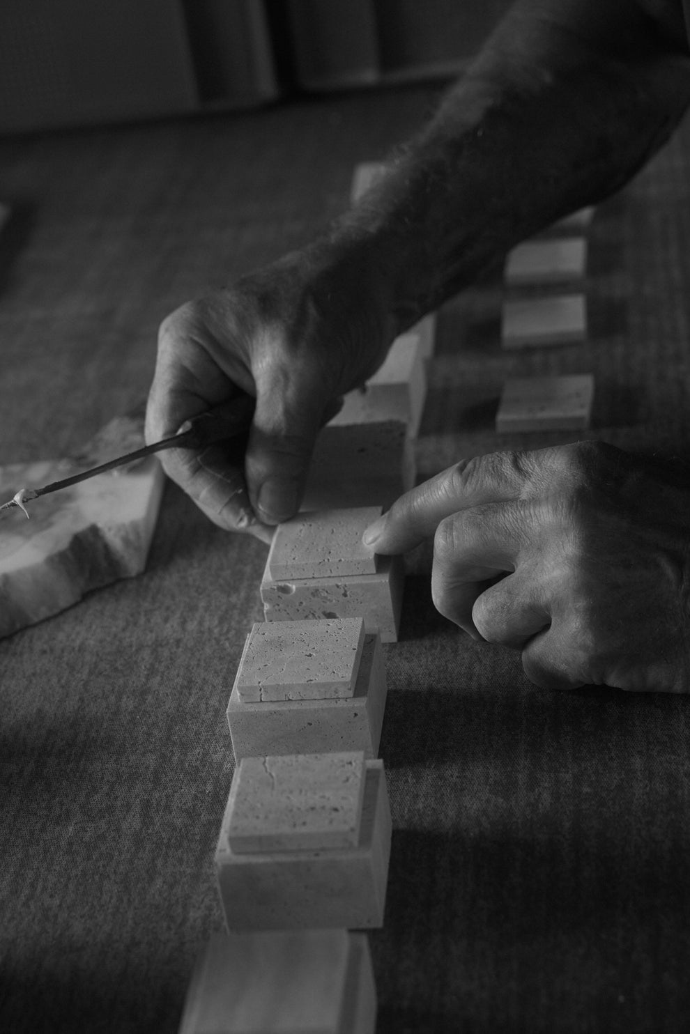 Man gluing a line of square travertin pieces together 