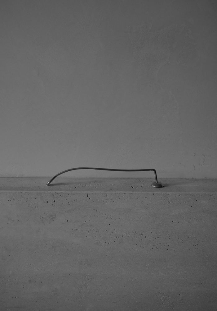 Silver Candle Stopper features an elegantly spiraled stainless steel handle, resting on a concrete slab, blending minimalist design with functional sophistication for extinguishing candles.