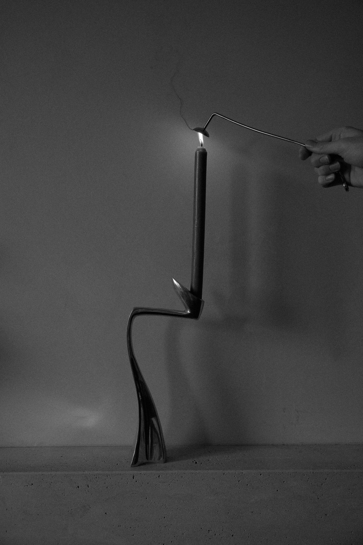 Silver Candle Stopper in a sculptural metal holder, twisting elegantly. A hand uses a tool to extinguish the flame, highlighting the holder's organic design.