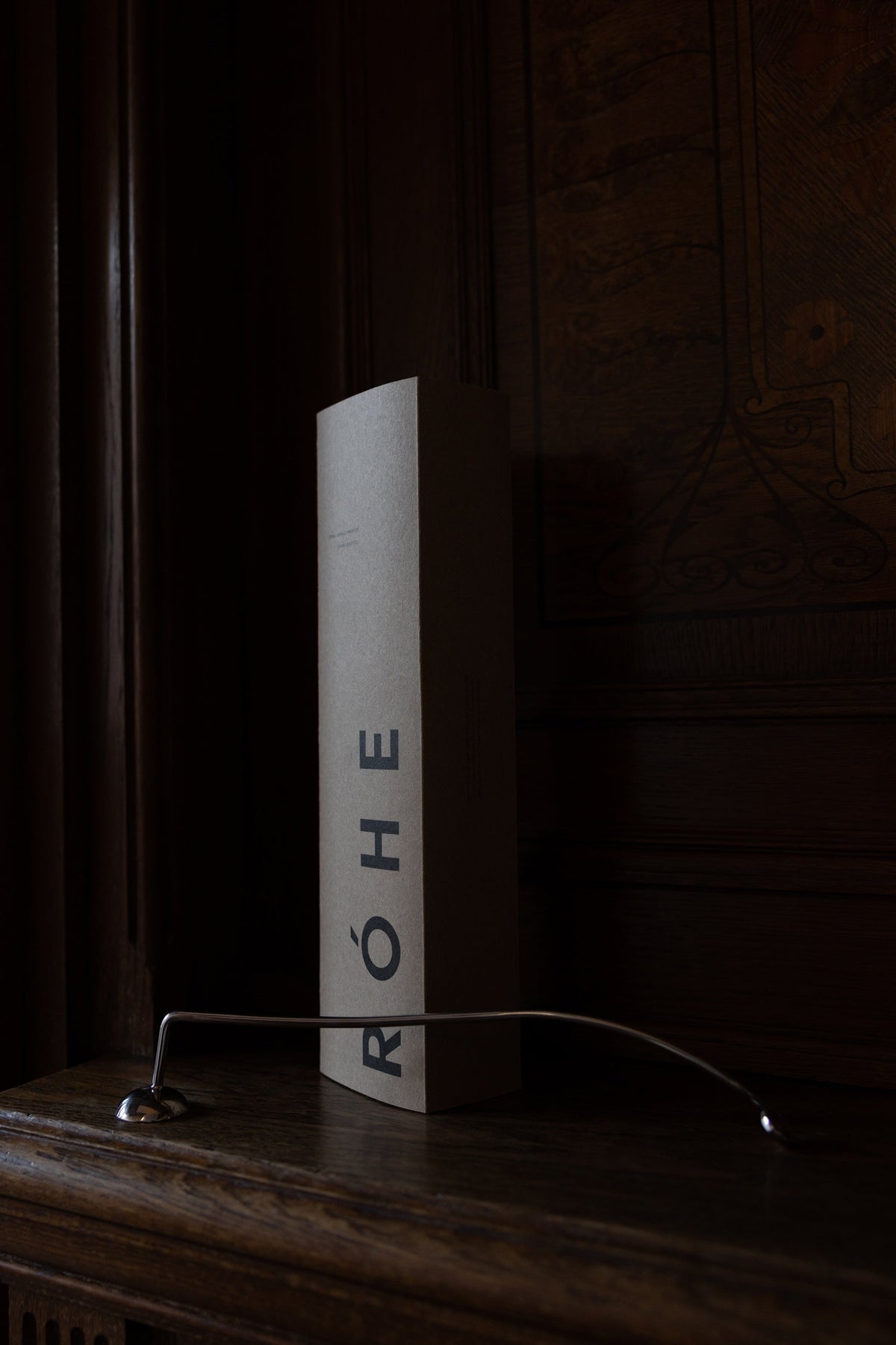 Candle Stopper | silver on a wooden mantel, featuring a curved stainless steel design with a spiraling handle, paired with its branded RÓHE packaging.