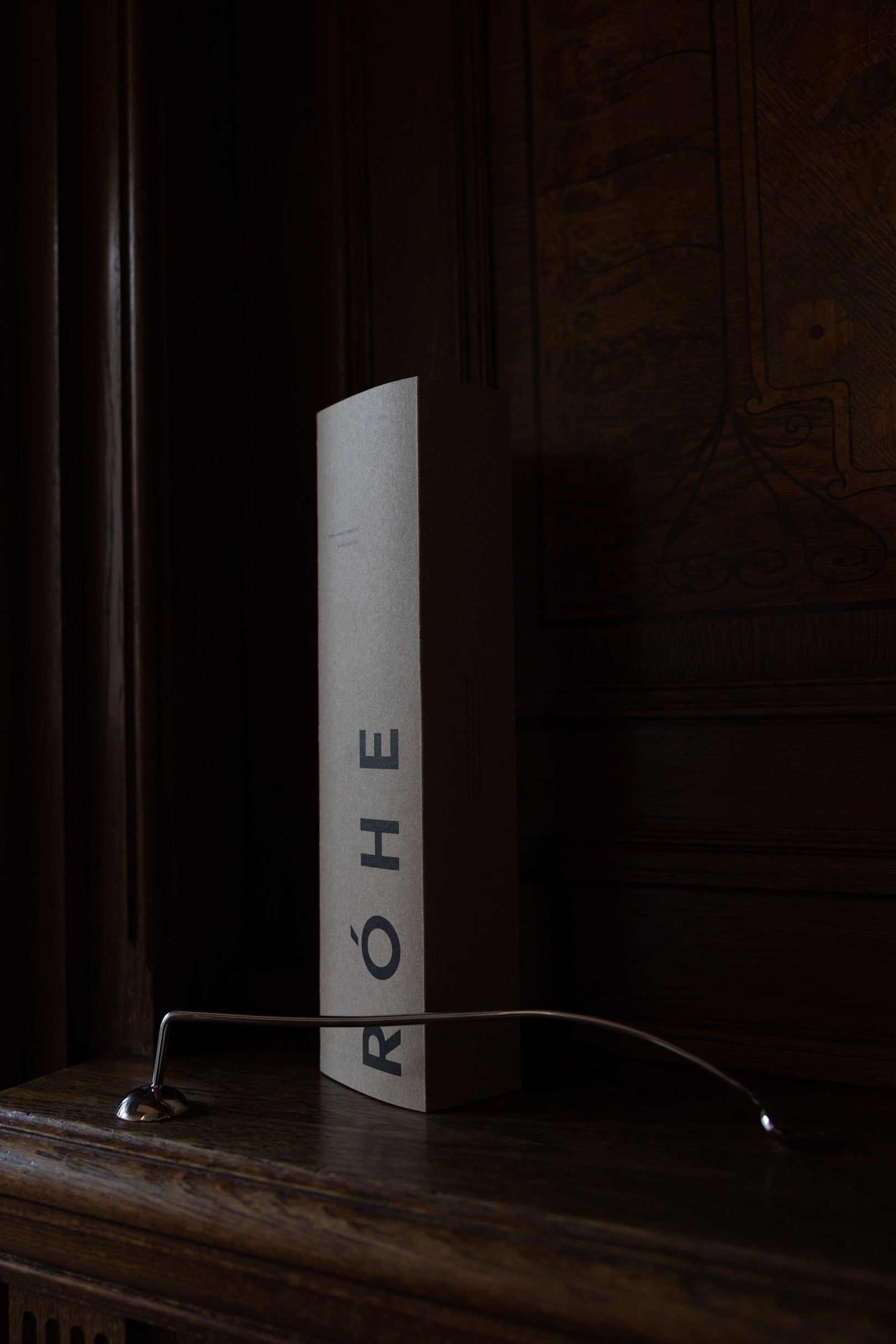 Candle Stopper | silver on a wooden mantel, featuring a curved stainless steel design with a spiraling handle, paired with its branded RÓHE packaging.