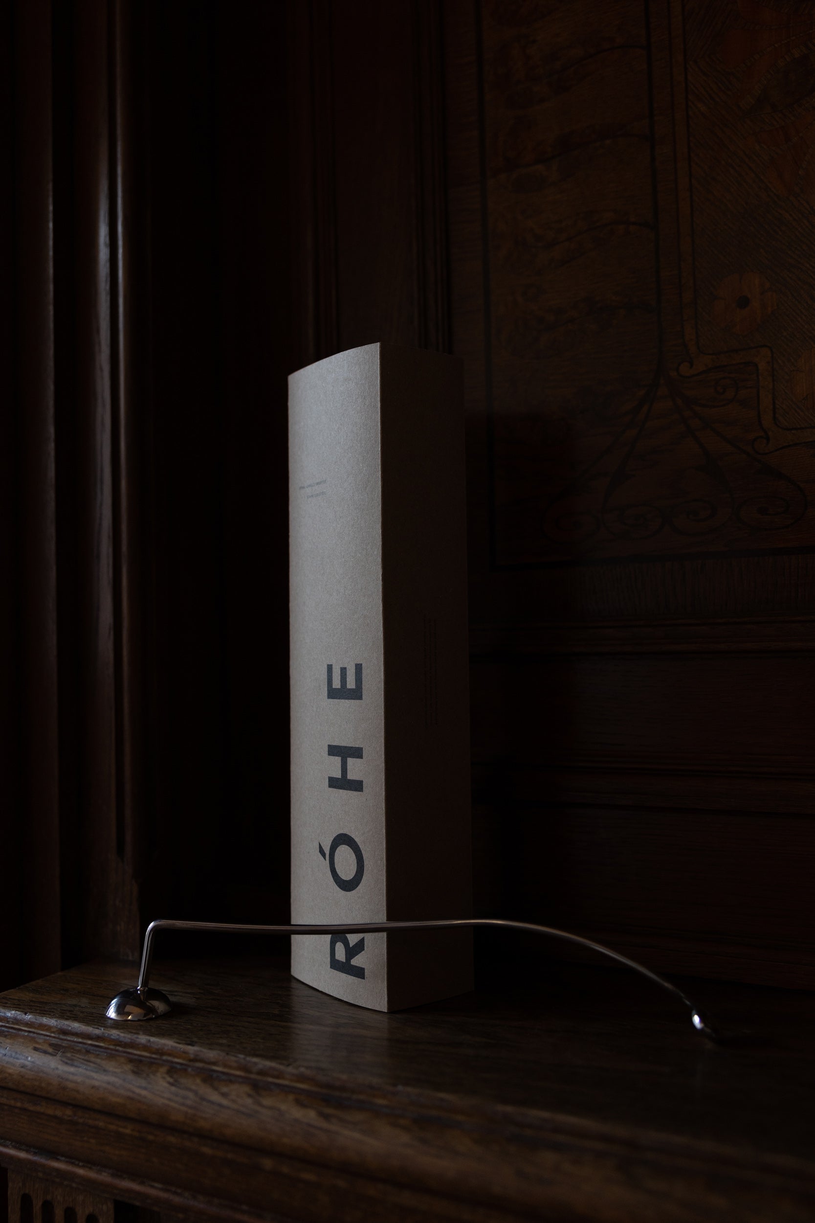 Candle Stopper | silver on a wooden mantel, featuring a curved stainless steel design with a spiraling handle, paired with its branded RÓHE packaging.