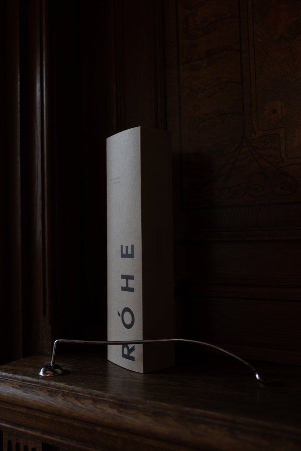 Candle Stopper | silver on a wooden mantel, featuring a curved stainless steel design with a spiraling handle, paired with its branded RÓHE packaging.