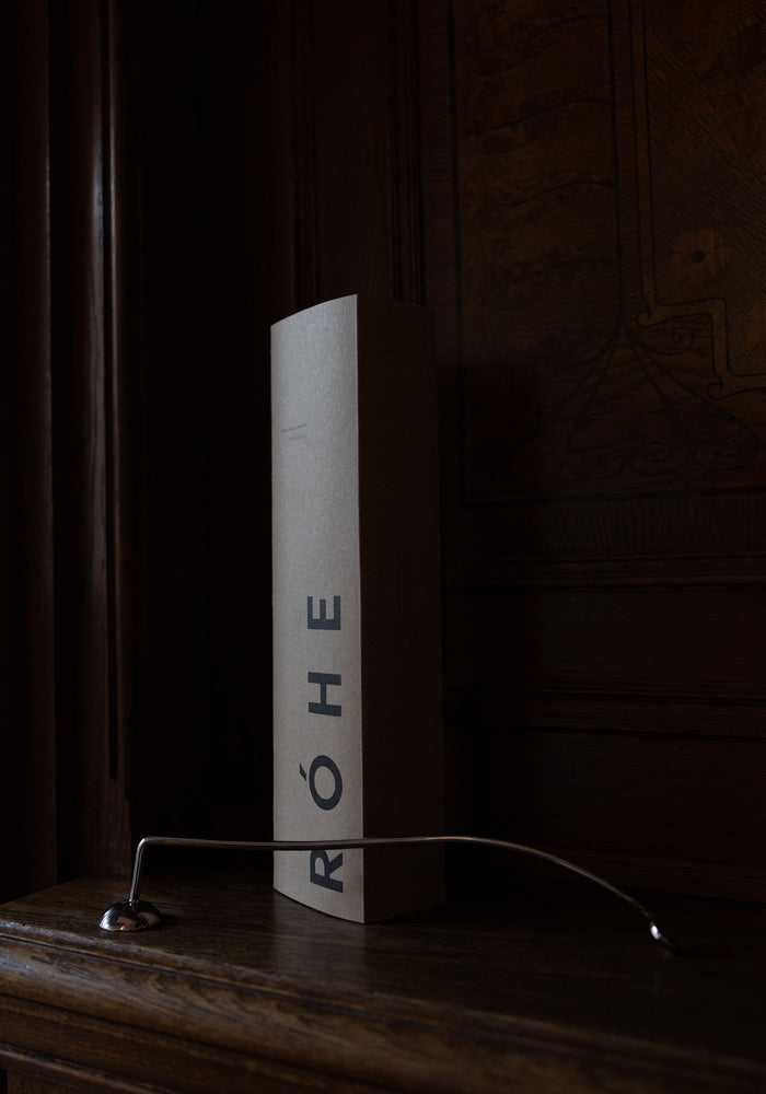 Candle Stopper | silver on a wooden mantel, featuring a curved stainless steel design with a spiraling handle, paired with its branded RÓHE packaging.