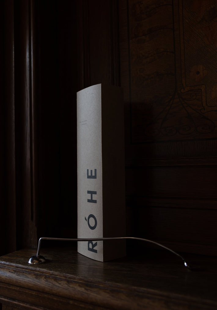 Candle Stopper | silver on a wooden mantel, featuring a curved stainless steel design with a spiraling handle, paired with its branded RÓHE packaging.