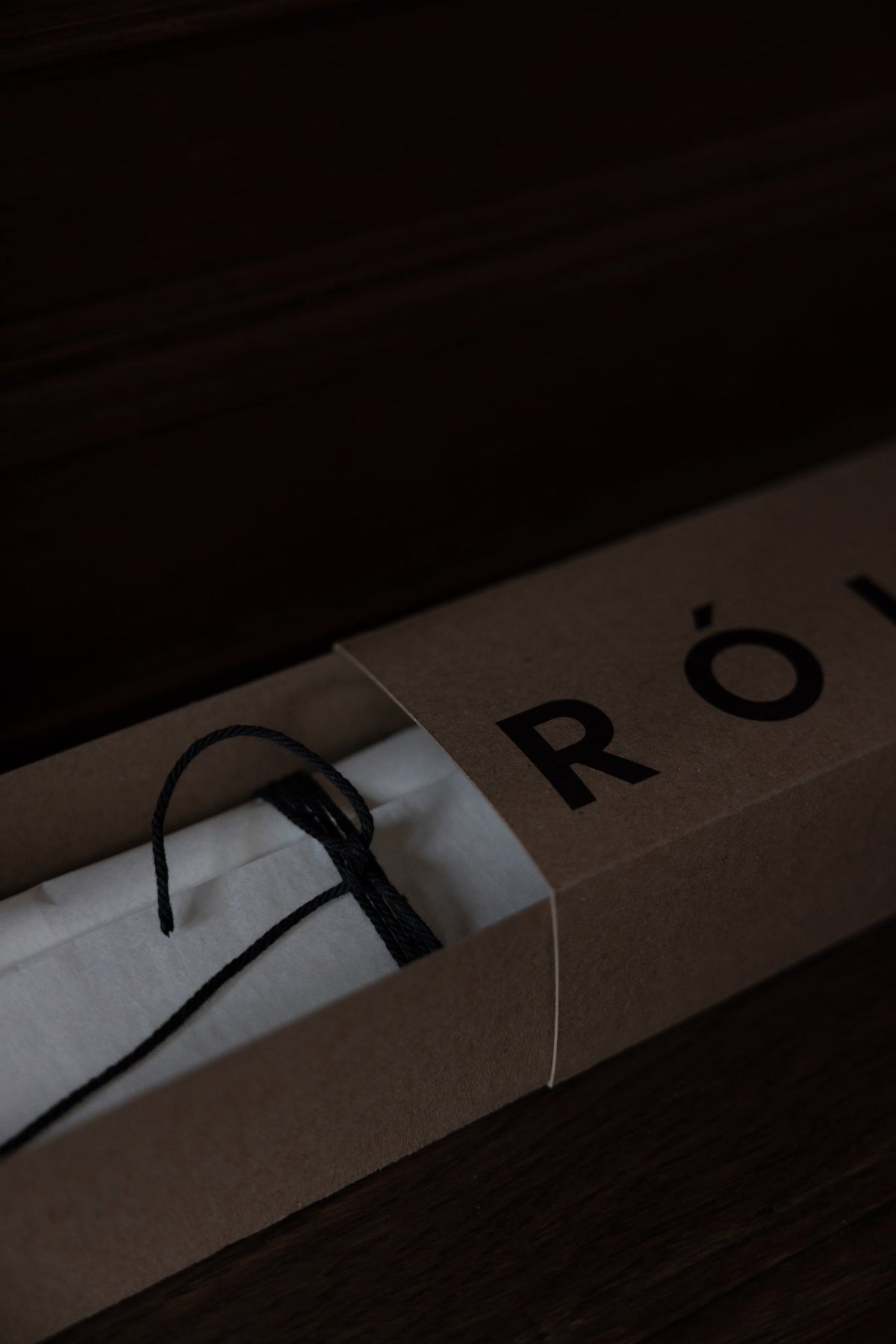 Kraft-paper box revealing a white tissue-wrapped item, likely the Candle Stopper | silver, tied with a black cord, partially showing “RÖ” logo.