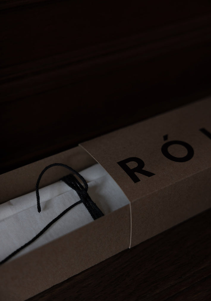 Kraft-paper box revealing a white tissue-wrapped item, likely the Candle Stopper | silver, tied with a black cord, partially showing “RÖ” logo.