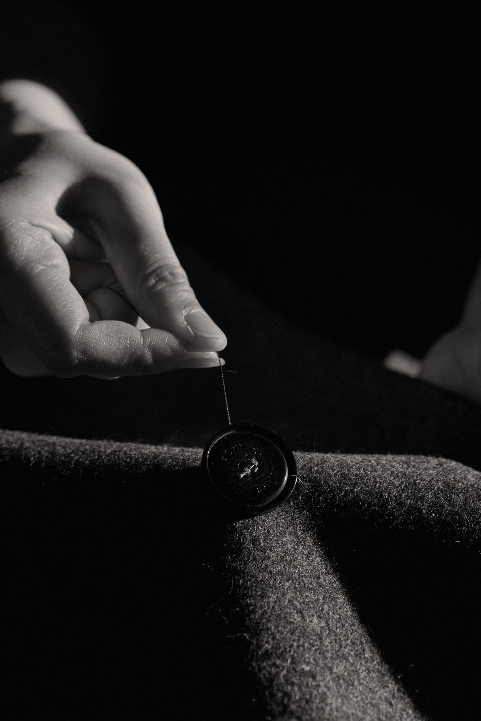 Hand using a needle to thread a button through fabric