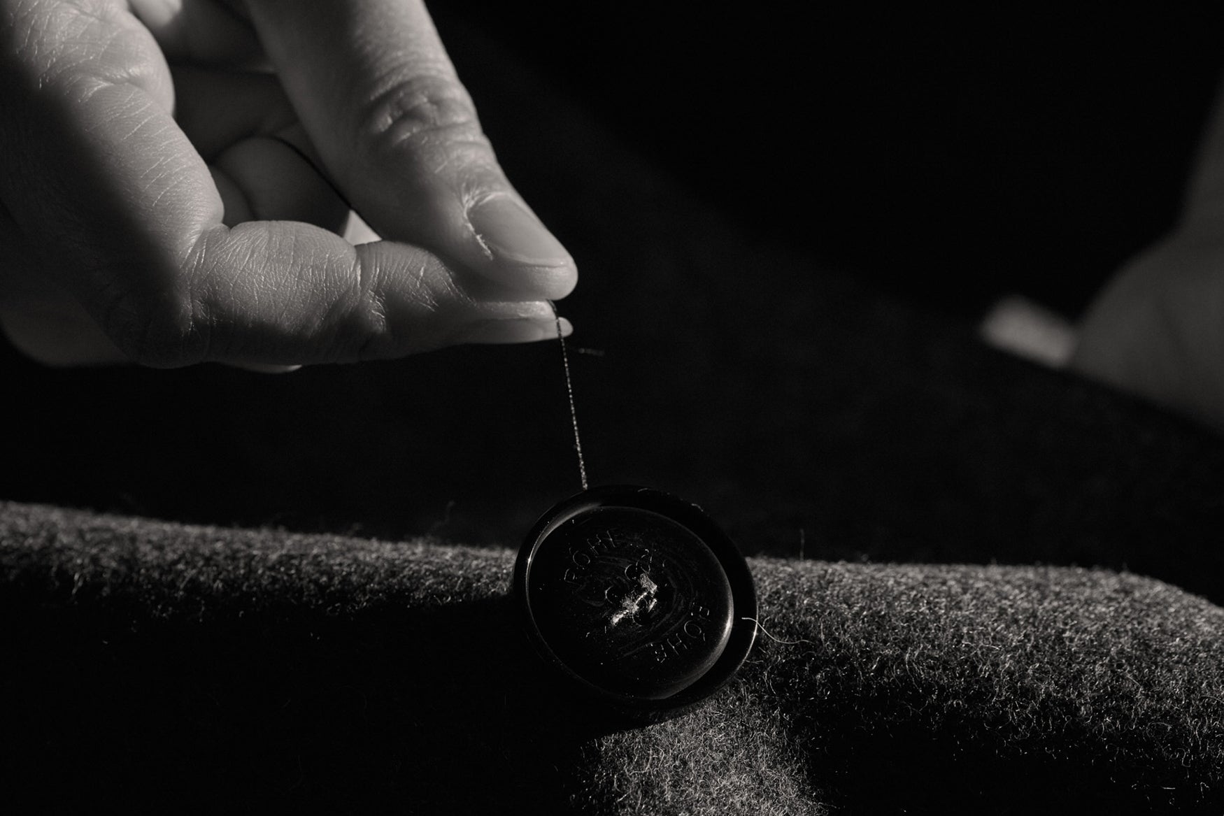 Black and white close-up of a hand sewing a button onto fabric.