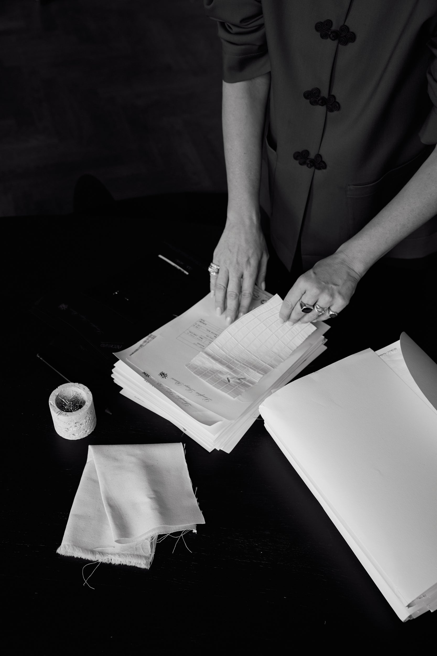 Hands sorting through papers and fabric swatches on a dark surface