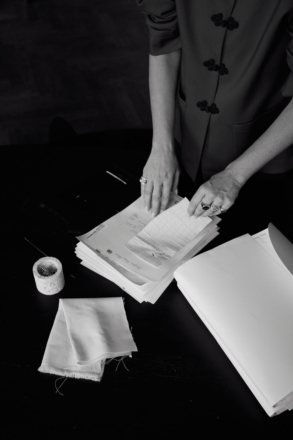Hands sorting through papers and fabric swatches on a dark surface