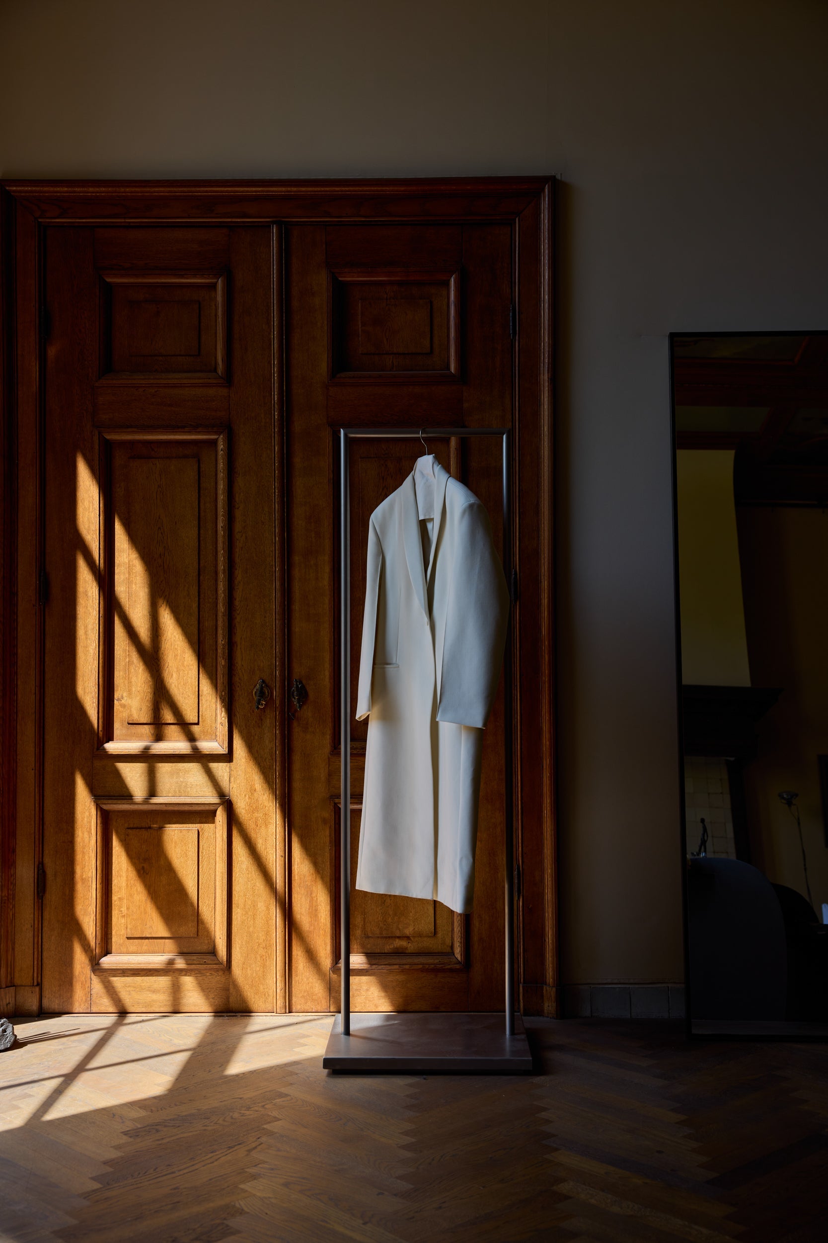 White coat hanging on a stand in a room with wooden floor and door and sunlight filtering through the windows