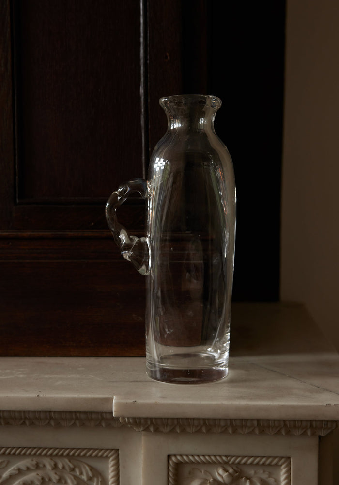 Large water carafe | Glass: A clear glass carafe with an ornamental handle, set on a marble shelf, showcasing Szkło Studio's unique, hand-blown craftsmanship.