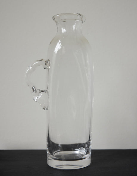 Large water carafe | Glass: A clear glass carafe with an ornamental handle, set on a marble shelf, showcasing Szkło Studio's unique, hand-blown craftsmanship.