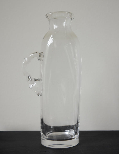 Large water carafe | Glass: A clear glass carafe with an ornamental handle, set on a marble shelf, showcasing Szkło Studio's unique, hand-blown craftsmanship.