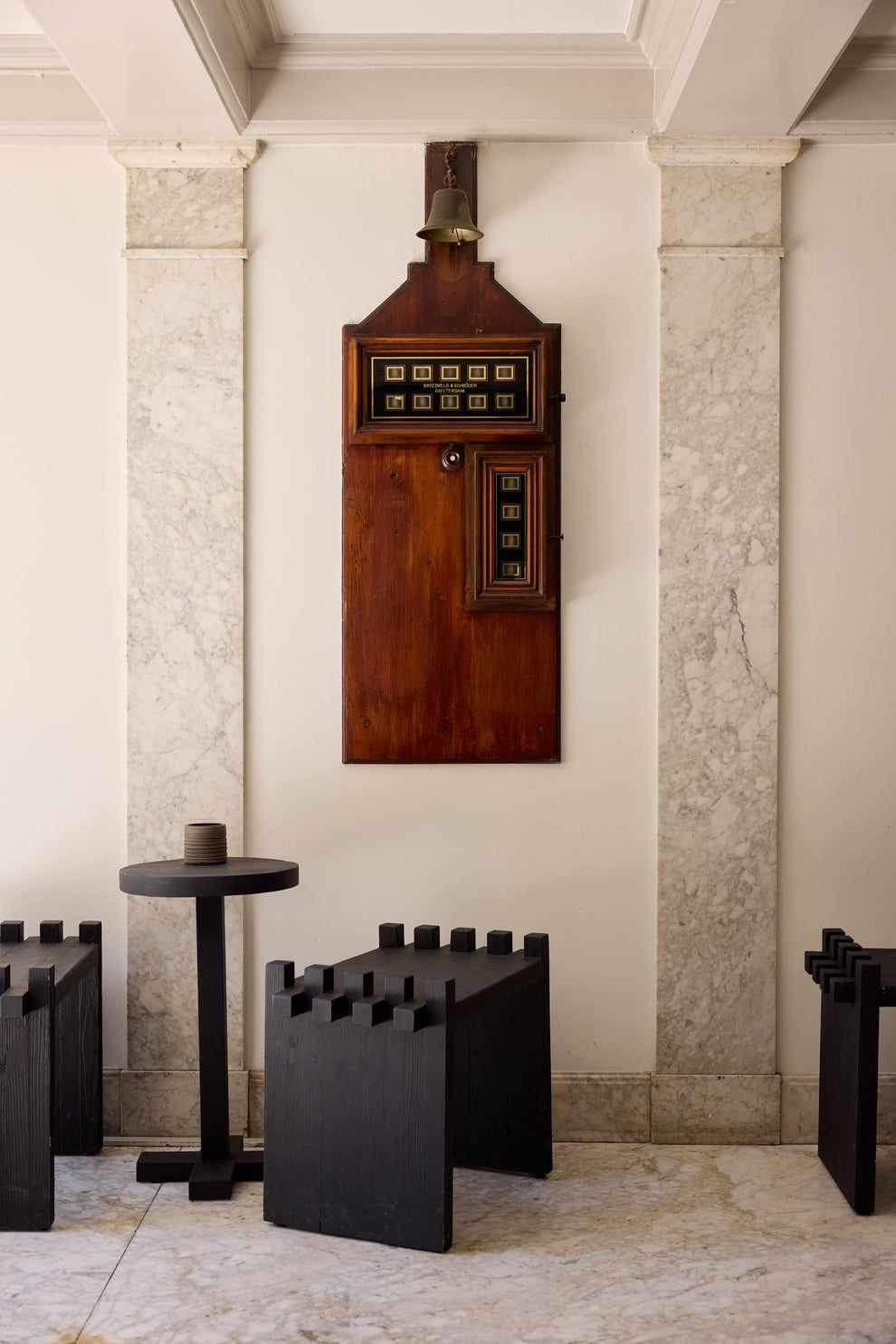 Vintage wooden payphone mounted on a stone wall with black stools below.