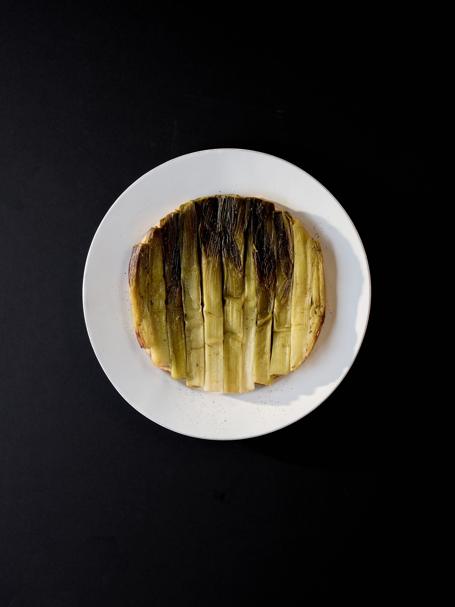 White plate with a leek tarte tatin on it against a black background
