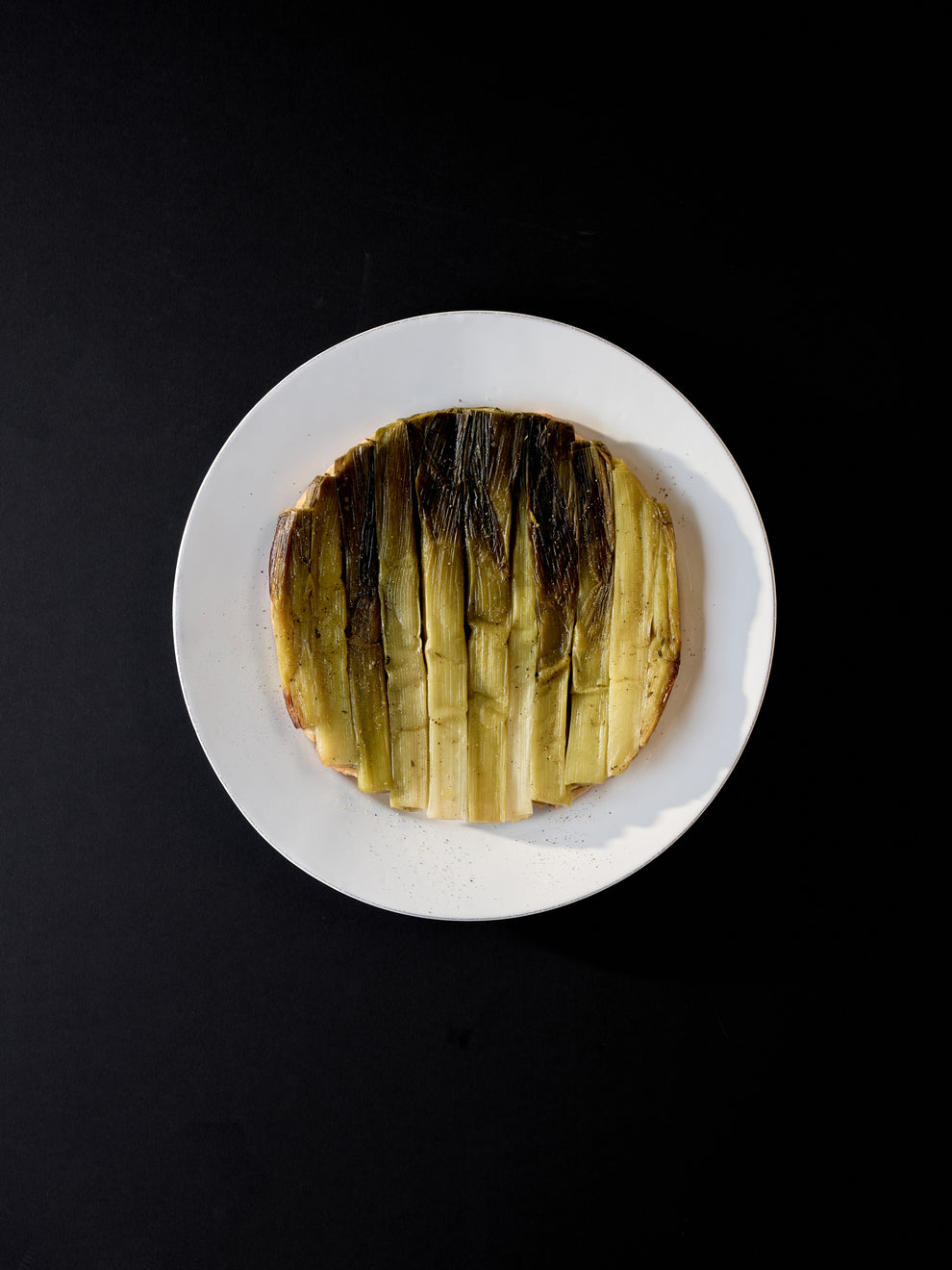 White plate with a leek tarte tatin on it against a black background