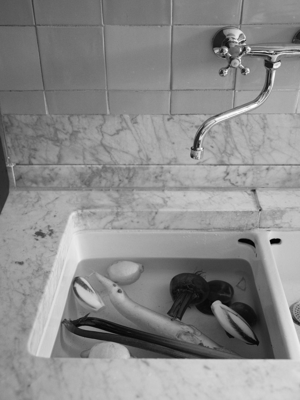 Various veggies laying in water in a 17th century sink with marble countertop