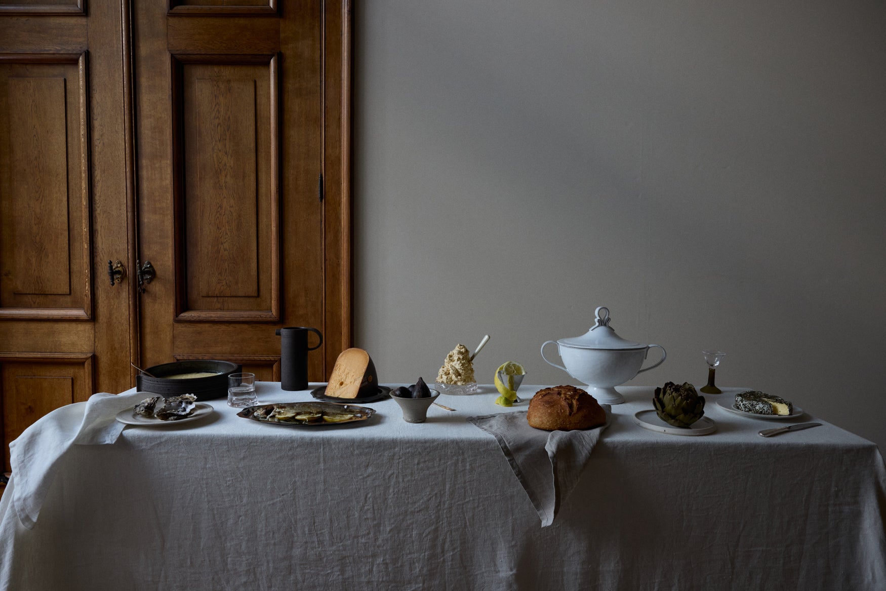 Table with white linnen tablecloth with various food on it like cheese, bread, a bowl of custard