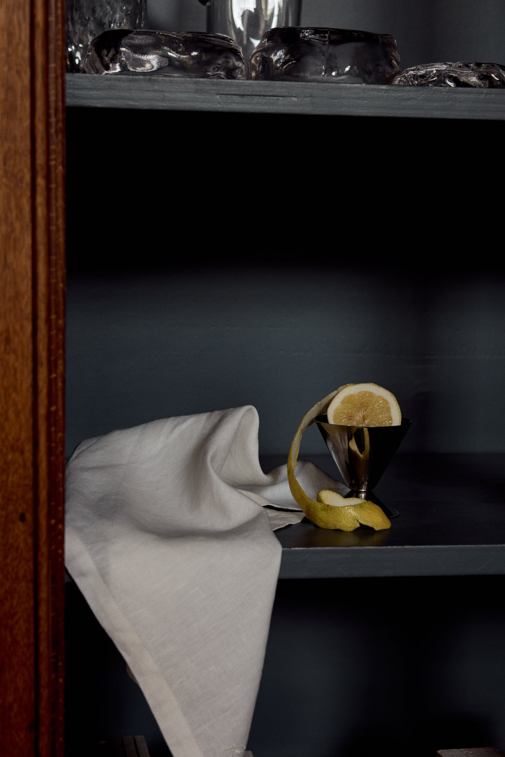 Shelf with a folded white napkin on it and a lemon peel draped around a silver coupe
