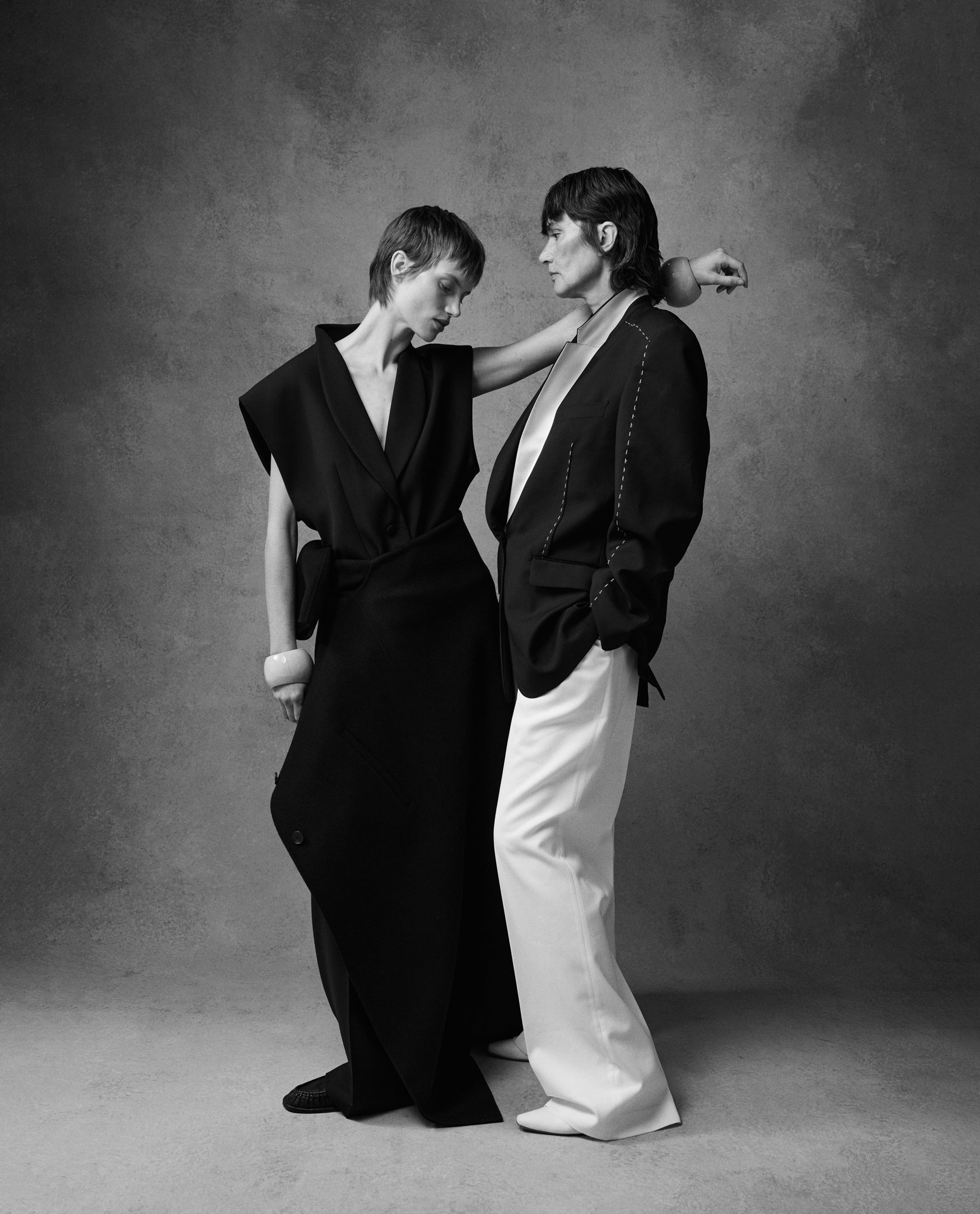 Two women, a daughter and mother, looking at each other in black outfits against a plain background
