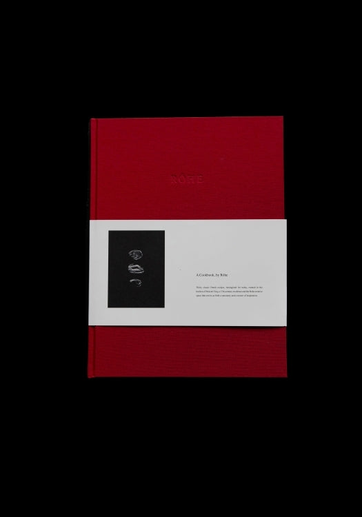 Front view of the Róhe Cookbook | red, a hardcover book with a deep red cover and a white paper band featuring minimalistic black and white artwork and text.