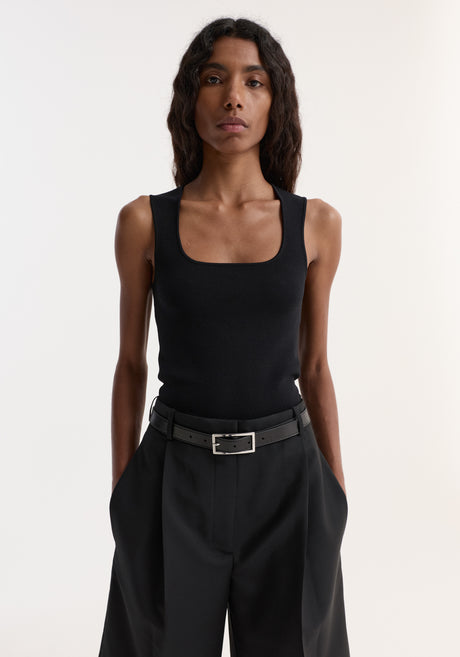 Woman in a Bustier shaped knitted top with a square neckline, paired with high-waisted tailored shorts and strappy sandals, showcasing a minimalist style.