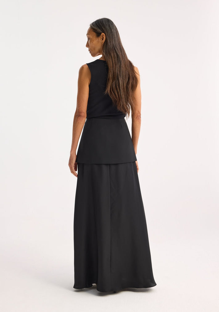 Woman in black ensemble showcasing Bustier shaped knitted top with a fitted silhouette; back view highlights flowing skirt-overlay, accentuating the top's bustier neckline design.