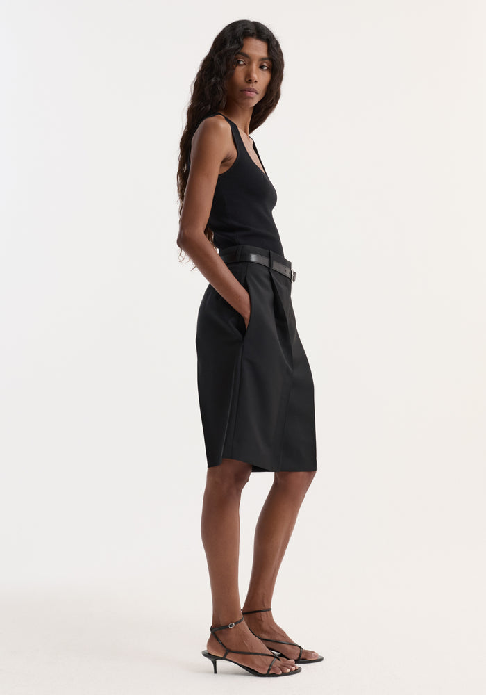 Woman in profile wearing a bustier shaped knitted top, sleeveless and fitted, paired with high-waisted shorts and heeled sandals.