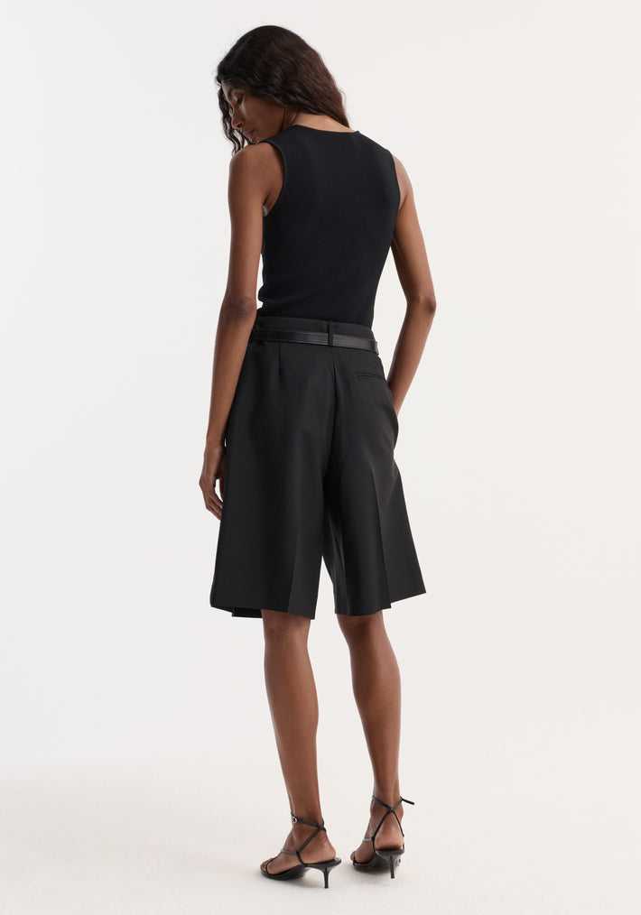 Woman in fitted black bustier-shaped knitted top and tailored shorts, standing with relaxed posture, showcasing the top's sleek, sleeveless design and flattering neckline.