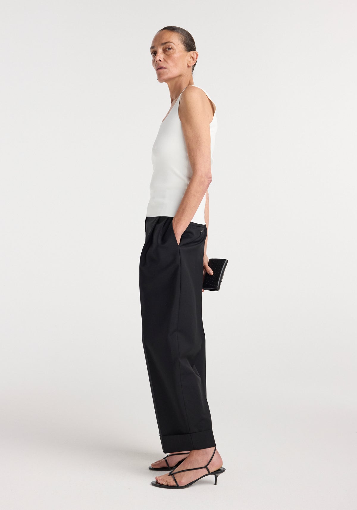 Woman wearing a sleeveless bustier shaped knitted top | optic white paired with high-waisted black wide-leg pants and strappy black sandals, holding a small black clutch.