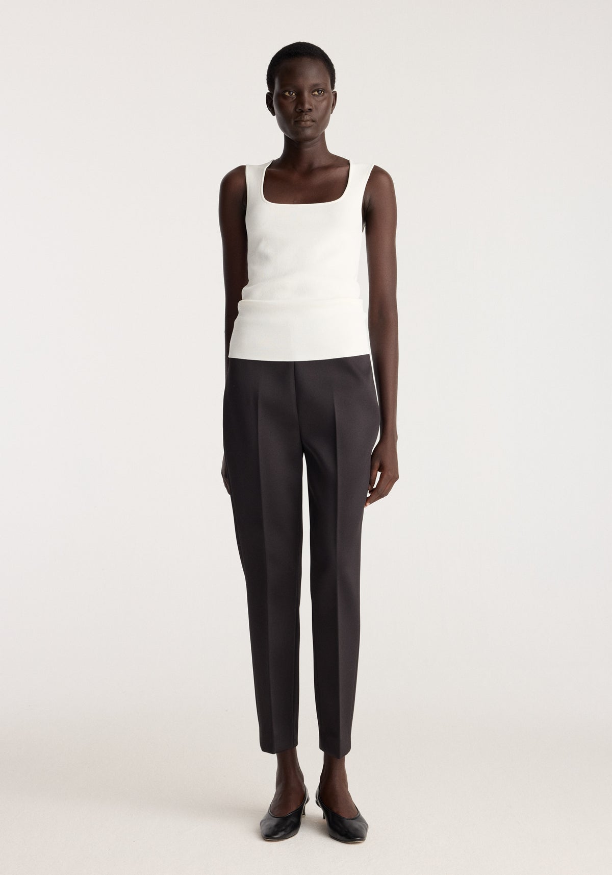 Model wearing Bustier shaped knitted top | optic white with black tailored trousers and black flats against a neutral studio background