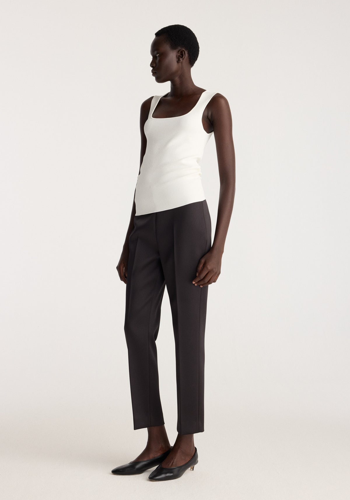 Bustier shaped knitted top | optic white worn with tailored black trousers and pointed black shoes on a model in a studio setting
