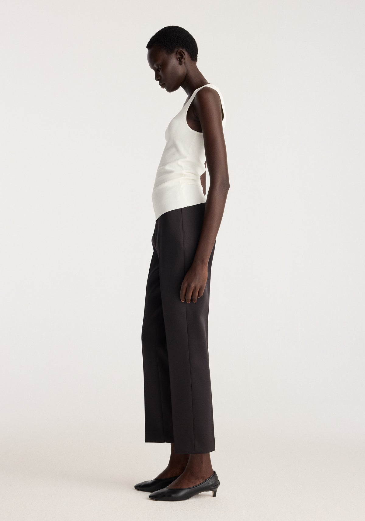 Bustier shaped knitted top | optic white shown on a model in profile with wide leg black trousers and pointed black heels