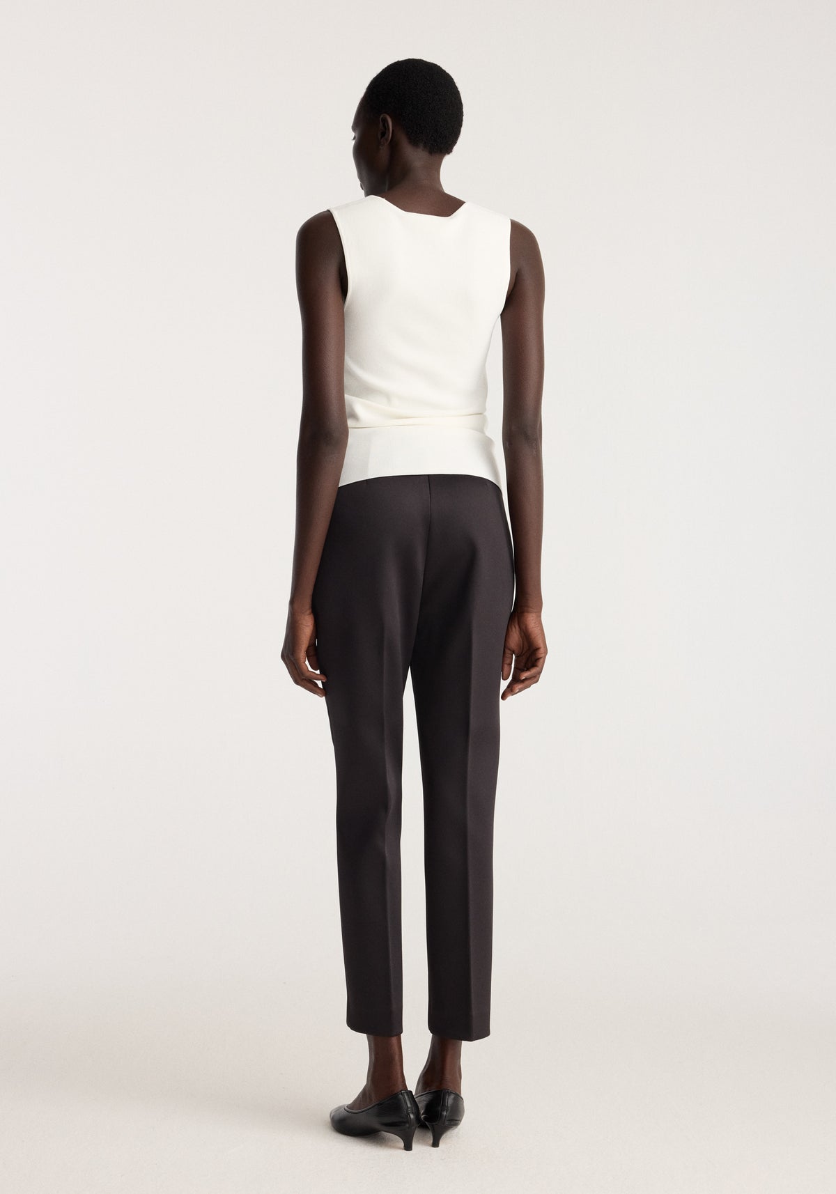 Bustier shaped knitted top | optic white shown from the back on a model with black trousers and black heels in a studio setting