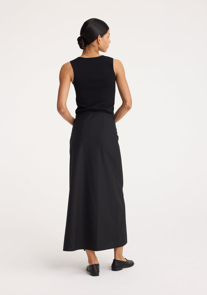 Woman in a sleeveless, fitted black Bustier shaped knitted top paired with a high-waisted skirt, showcasing the item's bustier neckline and sleek design.