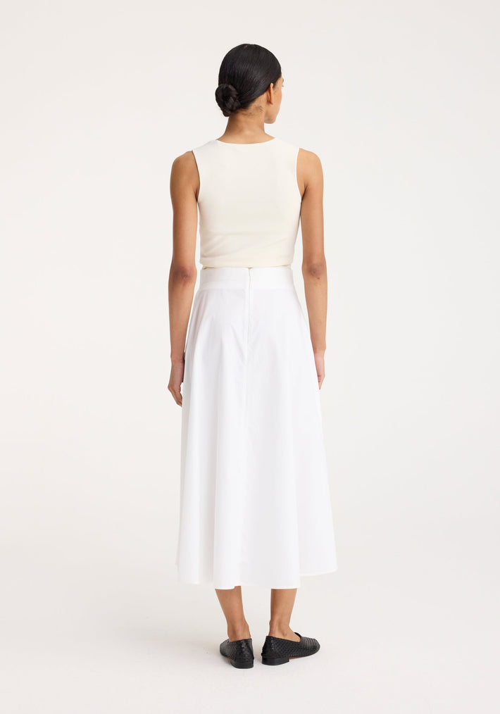 Woman in off-white bustier-shaped knitted top with fitted design, viewed from the back, paired with a high-waisted white skirt and black loafers.