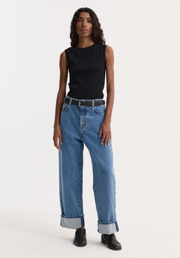 Model wears Dense rib tank top in black, showcasing its fitted style with mid-wash jeans, a black leather belt, and black slip-on shoes.