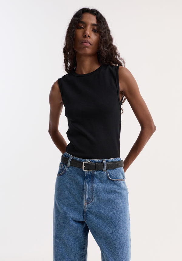 Model wearing Dense rib tank top | black, crafted from tight organic cotton and elastane, tucked into high-waisted blue denim jeans, showcasing a versatile, fitted look.