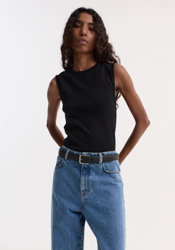 Model wearing Dense rib tank top | black, crafted from tight organic cotton and elastane, tucked into high-waisted blue denim jeans, showcasing a versatile, fitted look.