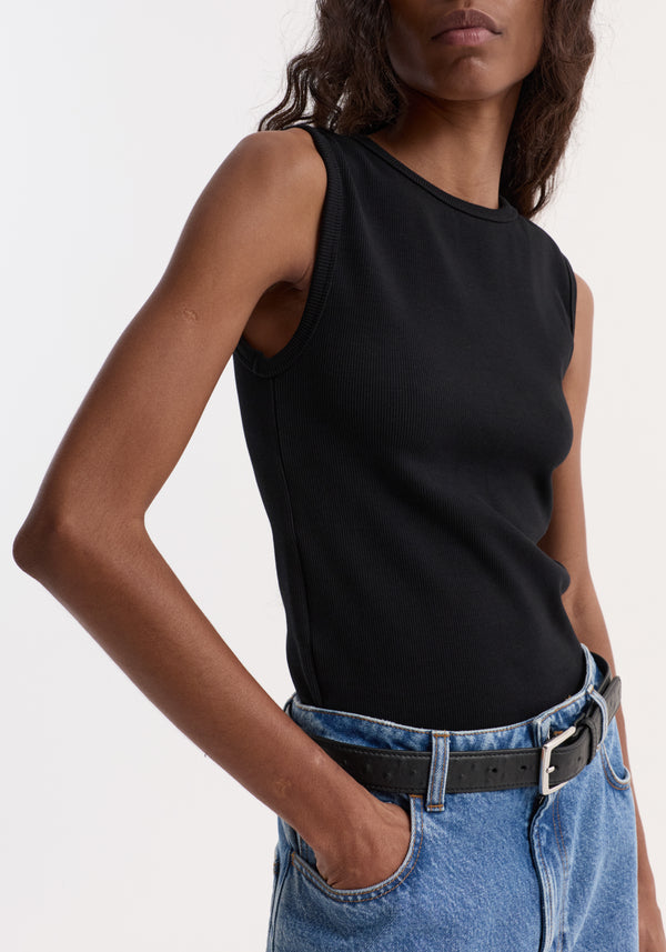 Dense rib tank top in black, fitted and sleeveless, tucked into high-waisted jeans with a black belt. Visible is the ribbed texture and elegant fit.