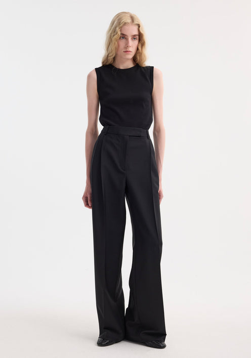 Slim individual wearing a Dense rib tank top in black, fitted and sleeveless, with high-waisted wide-leg trousers, showcasing minimalist fashion in a studio setting.