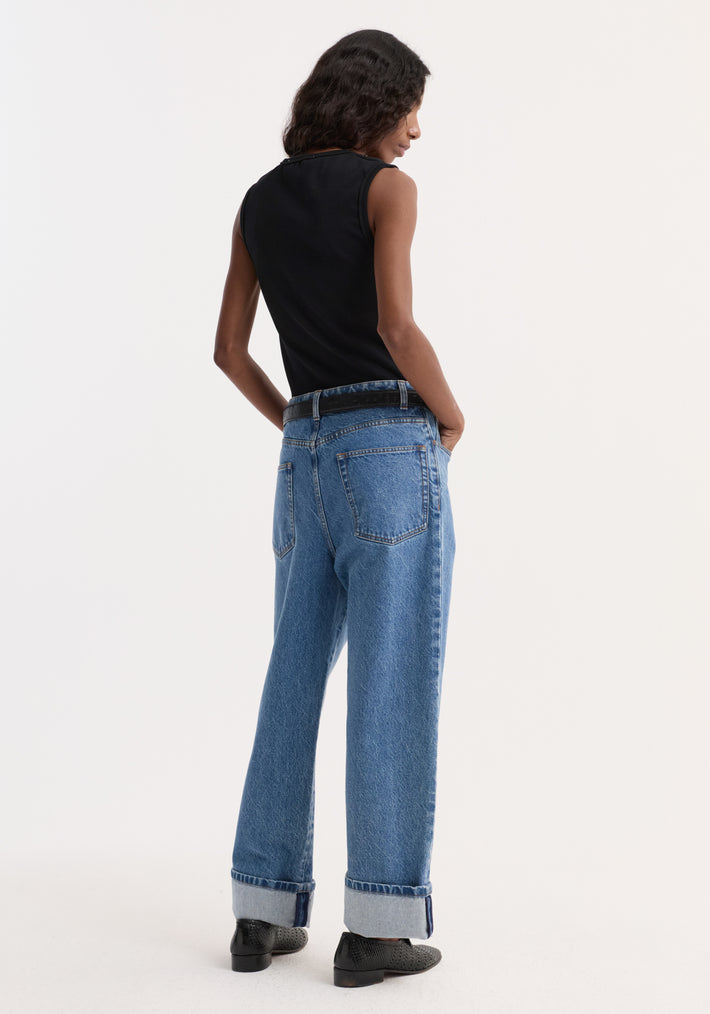 Model in dense rib tank top, black, tucked into high-waisted jeans with wide, cuffed legs. The tank is slim-fit, organic cotton, highlighting versatility.
