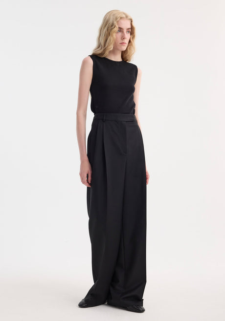 Slim individual wearing a Dense rib tank top in black, fitted and sleeveless, with high-waisted wide-leg trousers, showcasing minimalist fashion in a studio setting.