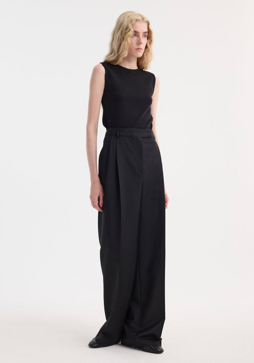 Slim individual wearing a Dense rib tank top in black, fitted and sleeveless, with high-waisted wide-leg trousers, showcasing minimalist fashion in a studio setting.