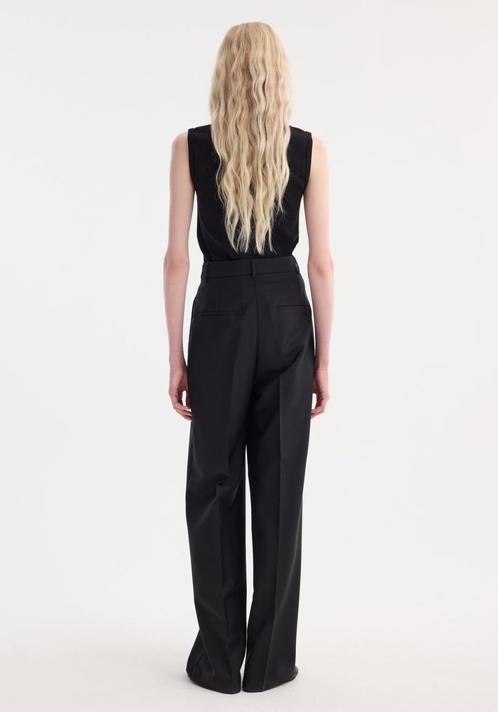 A person models the Dense rib tank top in black, showcasing its tight rib quality, sleeveless design, and comfortable fit with high-waisted wide-leg trousers.