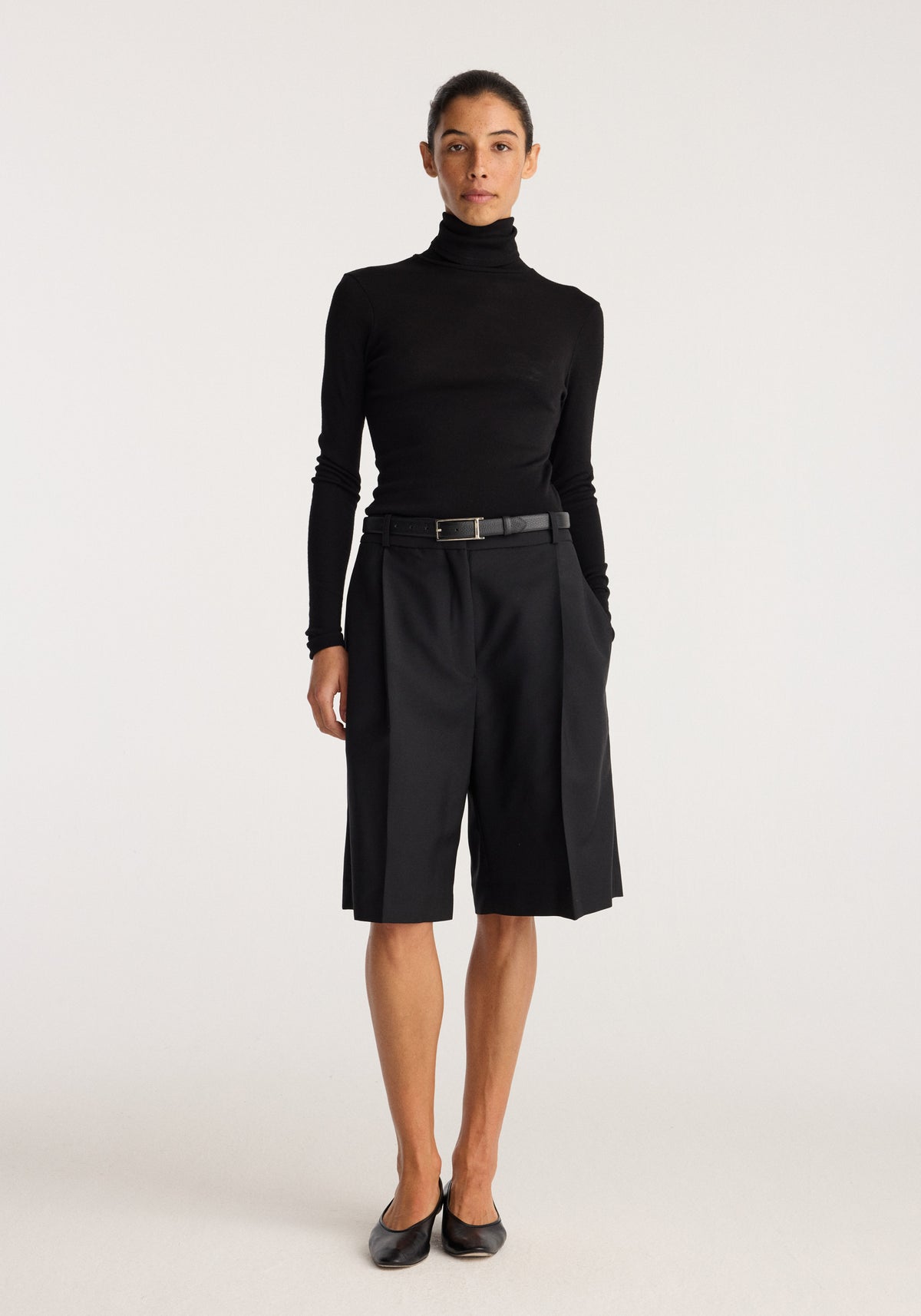 Fine merino turtleneck | black worn by a model with black tailored knee length shorts and loafers against a light neutral background