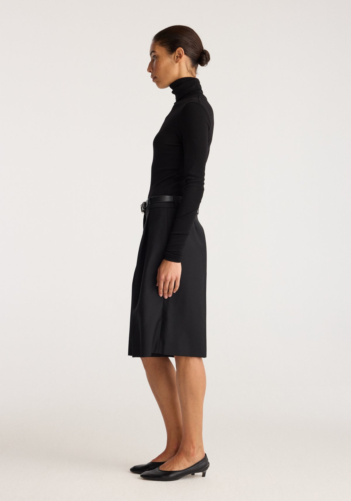 Fine merino turtleneck | black shown in side profile on a model with a fitted high neck and long sleeves styled with a black skirt and heels